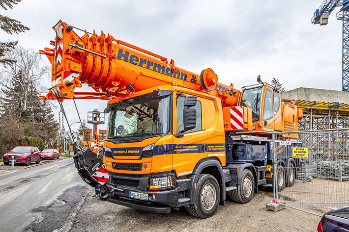 Telescopic truck-mounted crane hoists work platform through a gym roof