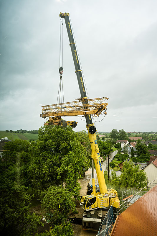 Mobile crane lifts construction crane over treetops