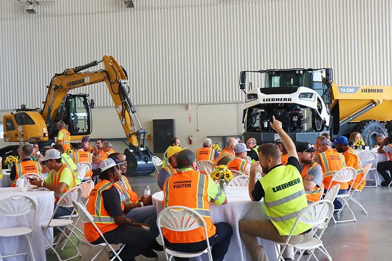 Customers enjoying  a barbecue lunch at the Liebherr Equipment Source open house event at the Liebherr USA, Co. Newport News, VA campus. Liebherr crawler excavator and articulated dump truck shown in the background.