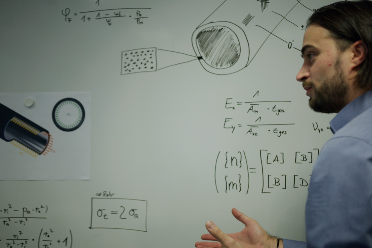 Ein Mann steht vor einer Tafel mit mathematischen Lösungen für die Entwicklung von Hydraulikzylindern von Liebherr