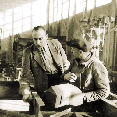 Close up of Hans Liebherr speaking to a colleague in a factory 