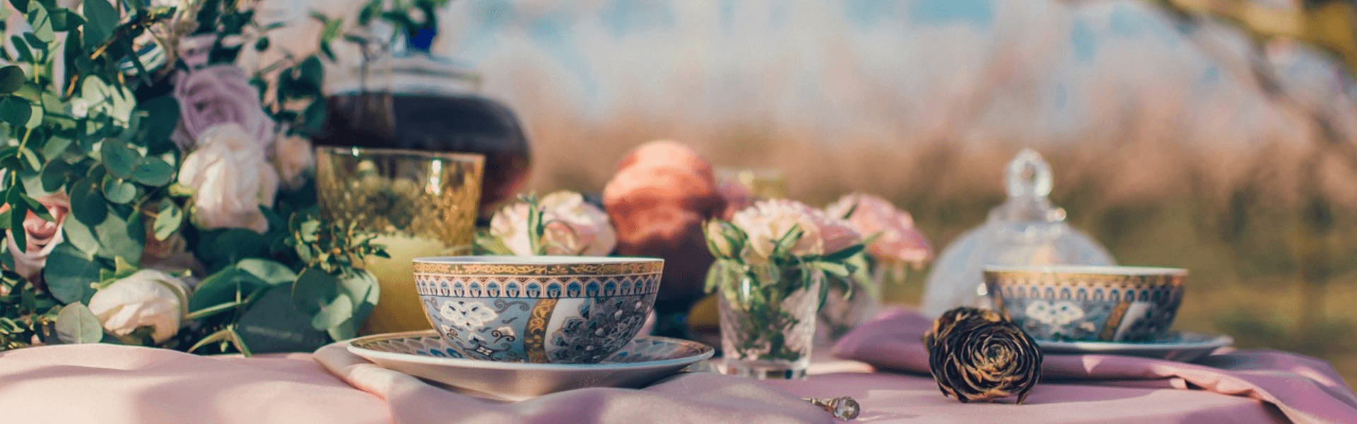 Afternoon tea set on a pink tablecloth outdoors, with a whimsical garden in the background and fresh flowers adorning the table
