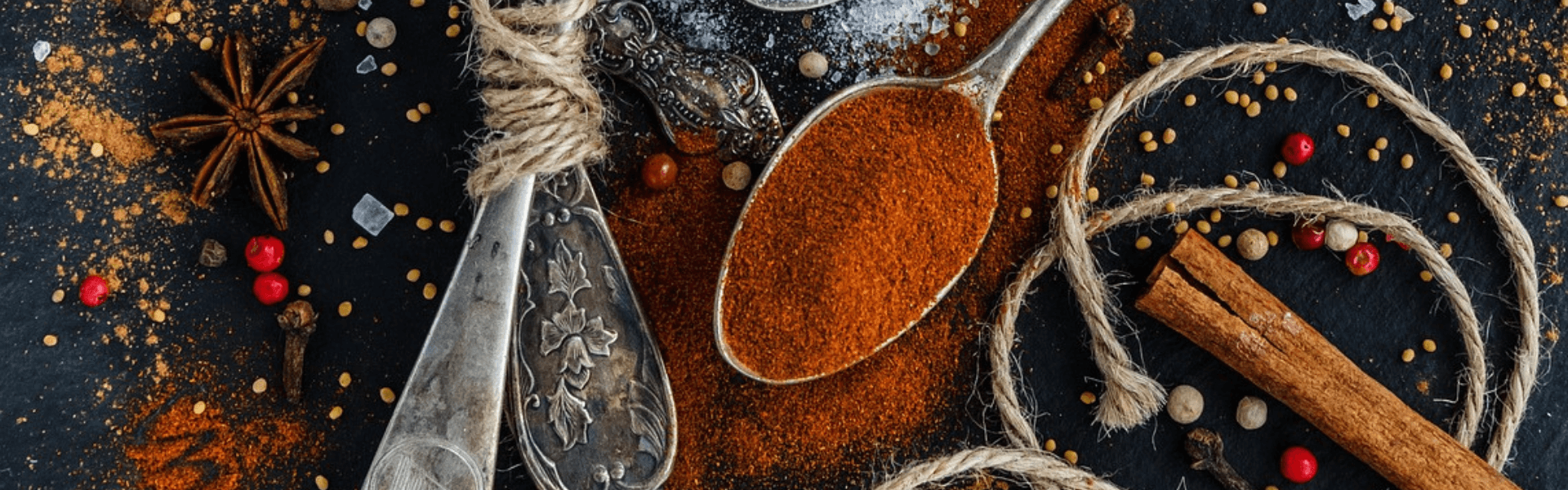Assortment of spoons with various herbs, scattered herb dustings, and a piece of yarn on a dark board