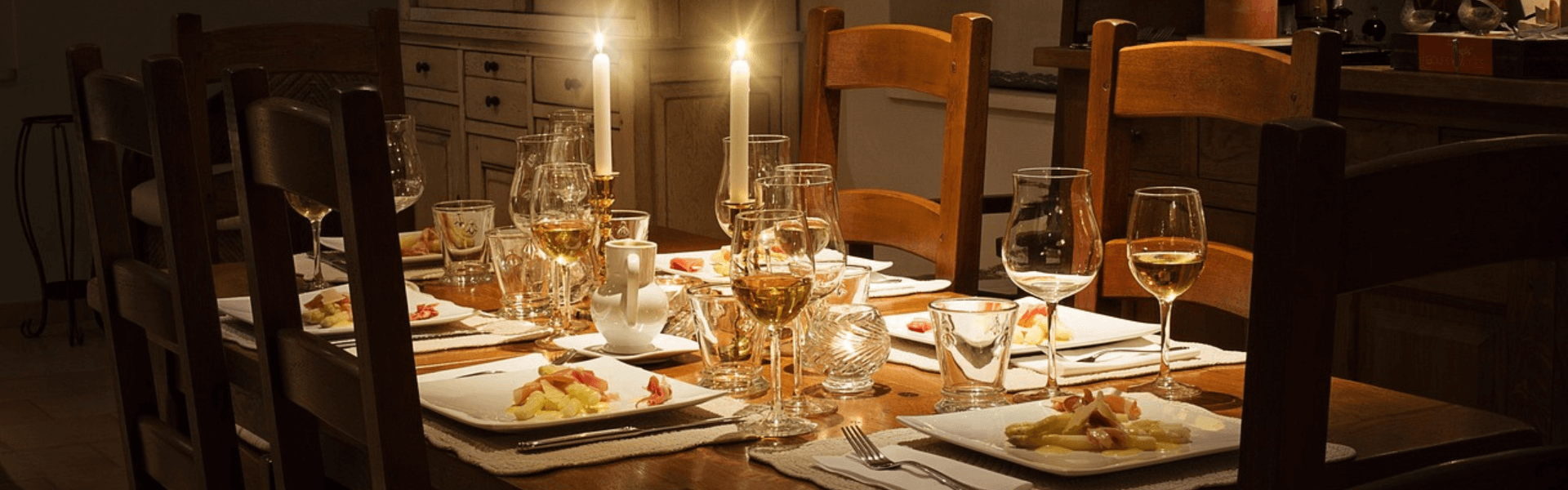 Dining table Candlelit dining table set for dinner with serving plates, the soft shadows and warm glow drawing attention to the table in a dimly lit room.