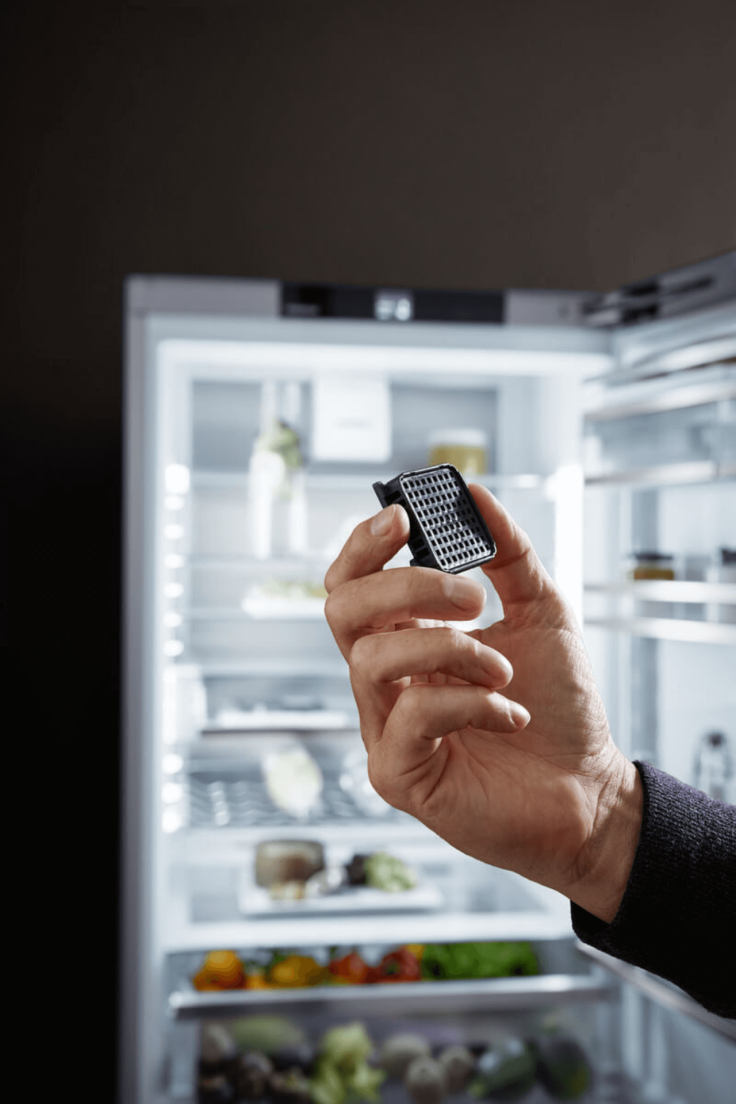 Close up of a person holding a charcoal filter with an open door fridge behind the charcoal filter