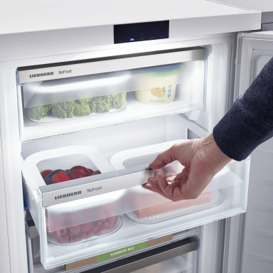 close up of a persons hand pulling out a drawer in a small freezer