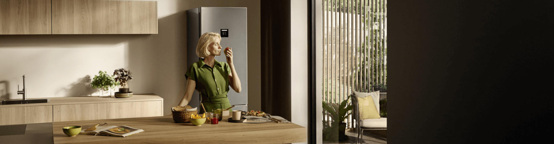 Close-up of a woman smelling a pear in a modern kitchen, with a fridge freezer visible in the background.