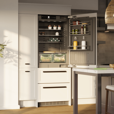 Built-in Liebherr refrigerator installed in a modern kitchen, shown with the door open to reveal organised shelves, door storage, and two transparent vegetable drawers filled with fresh produce.
