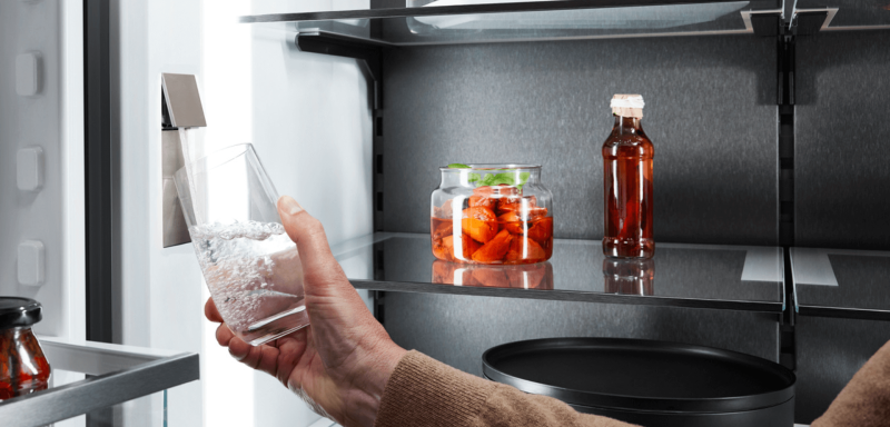 Close-up view of an open BlackSteel French Door refrigerator, showing a person's hand using the InfinitySpring to dispense fresh water.