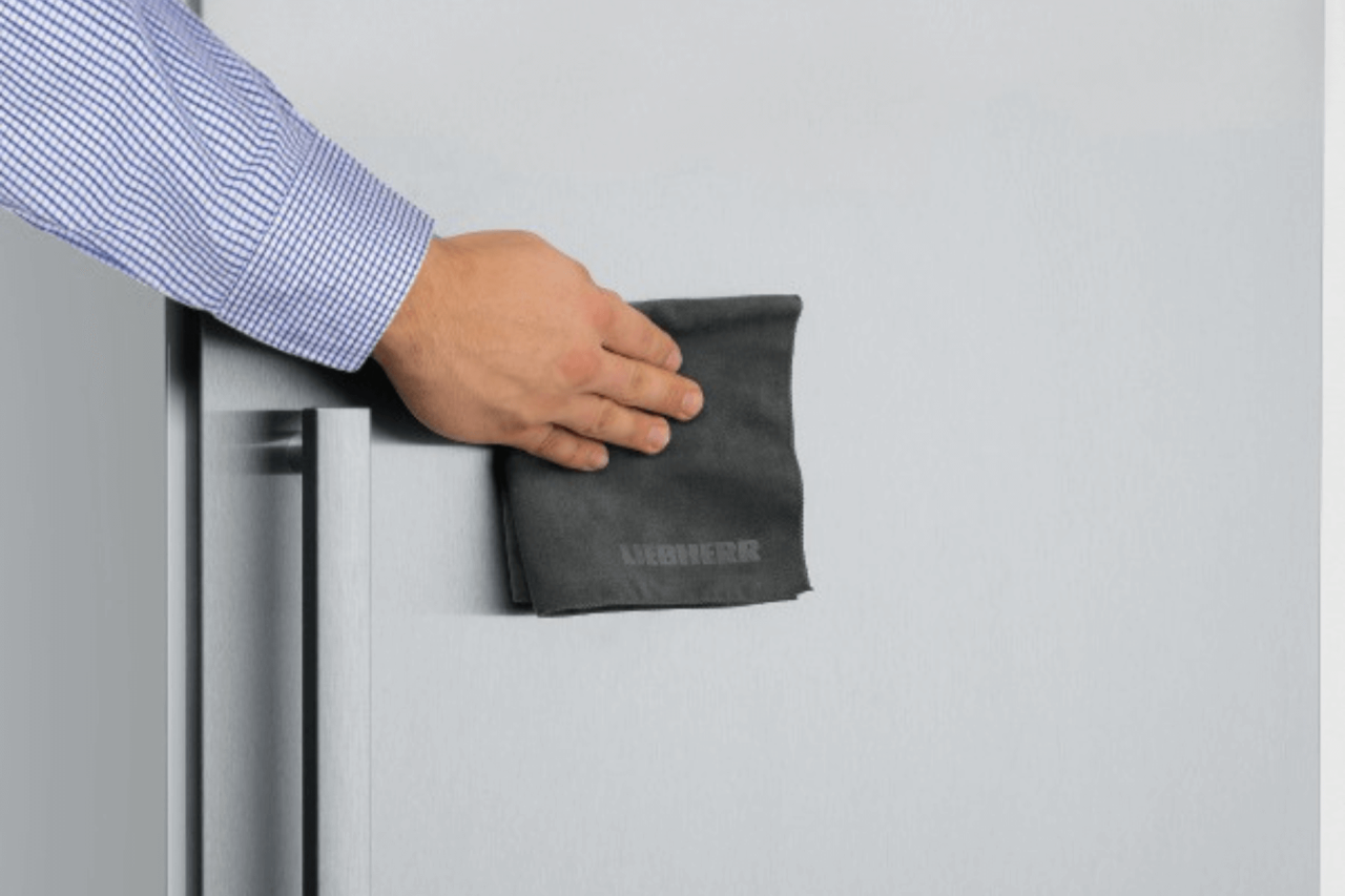 Close up of a persons hand wiping an appliance with a cloth