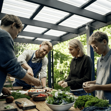 Mikkel Karstad and his family preparing fresh food together around an outdoor table.
