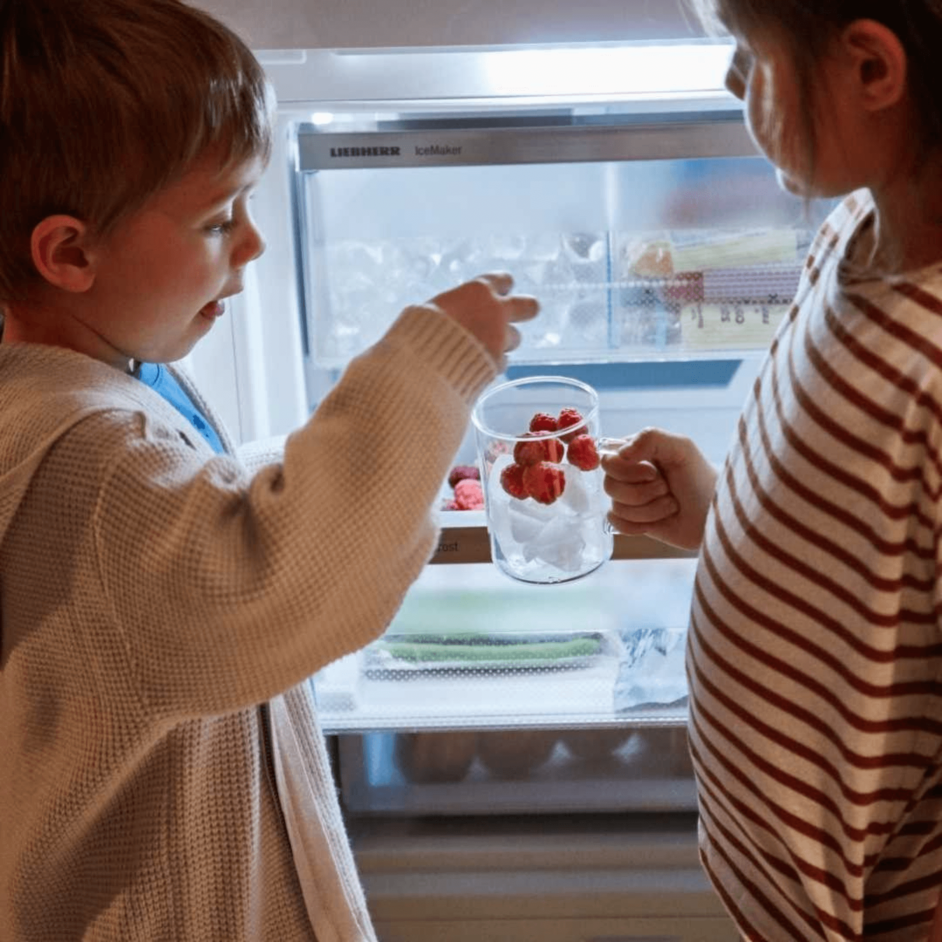 Children placing frozen berries into cups in front of NoFrost drawer freezer