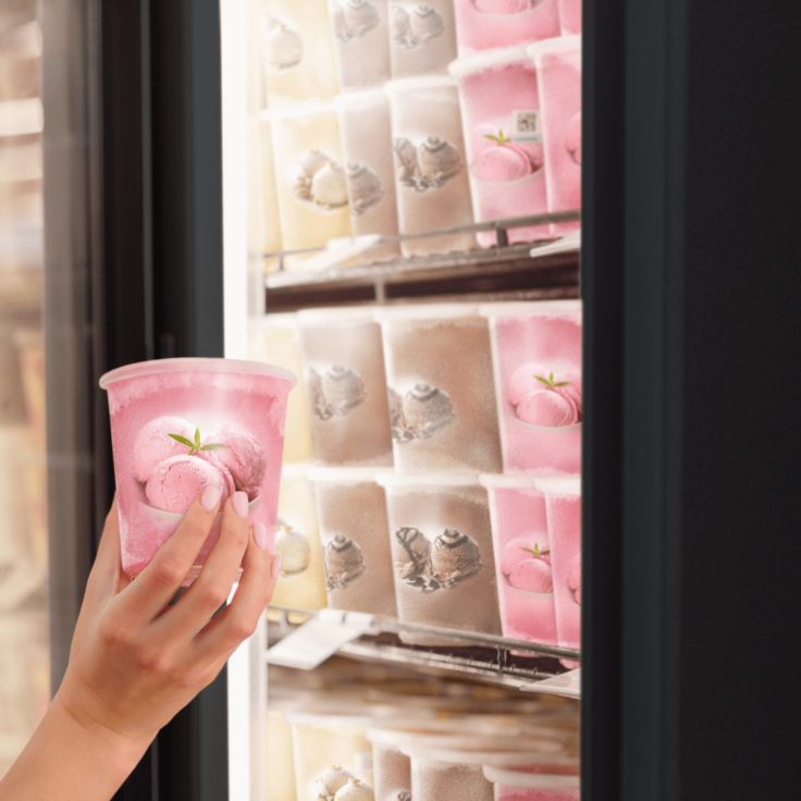 Woman holding a tub of ice cream that she took out of a large freezer in a supermarket