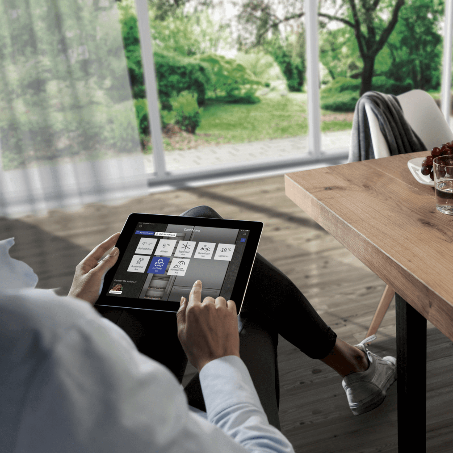 Person sitting at a dinner table with their leg crossed whilst they sit on a tablet changing settings of their appliance