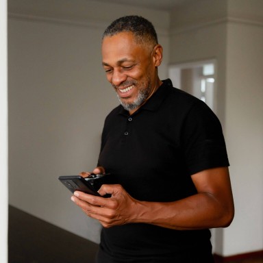 Man smiling while looking down at his phone holding a thermos mug