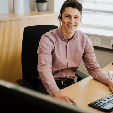 Liebherr professional staff member looking at the camera smiling whilst working on a computer with a headset on