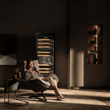 Woman drinking wine in front of her Liebherr wine fridge relaxing