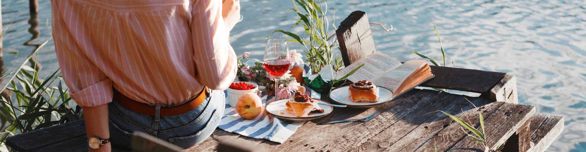 Woman turned towards the beach drinking wine whilst reading a book