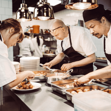 Chefs plating dishes in a busy professional kitchen environment.