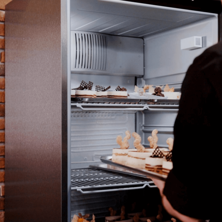 Close up of an open fridge with a chef putting dessert on the shelves