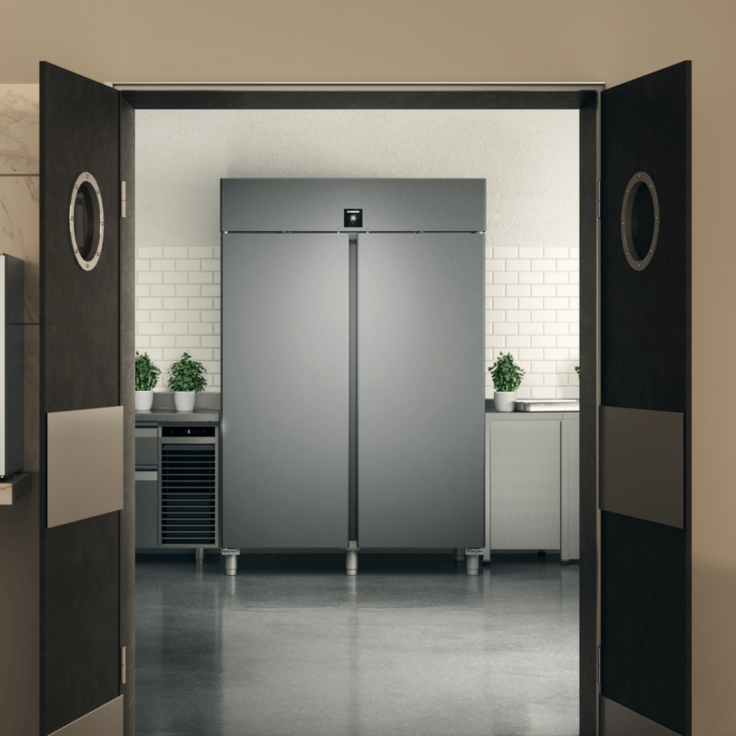 Large fridge in a restaurant with the service doors to the kitchen open showcasing the appliance 