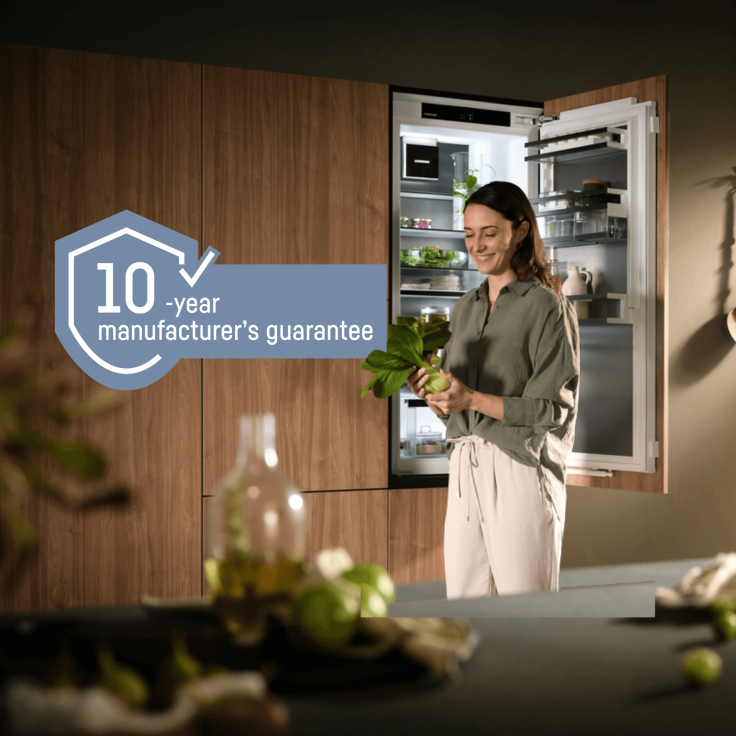 Integrated fridge with BioFresh; a woman stands by an open fridge, holding and looking at a leek. Includes a 10-year guarantee logo, representing a free 10-year guarantee on all household appliances from 1st May to 31st October 2026.