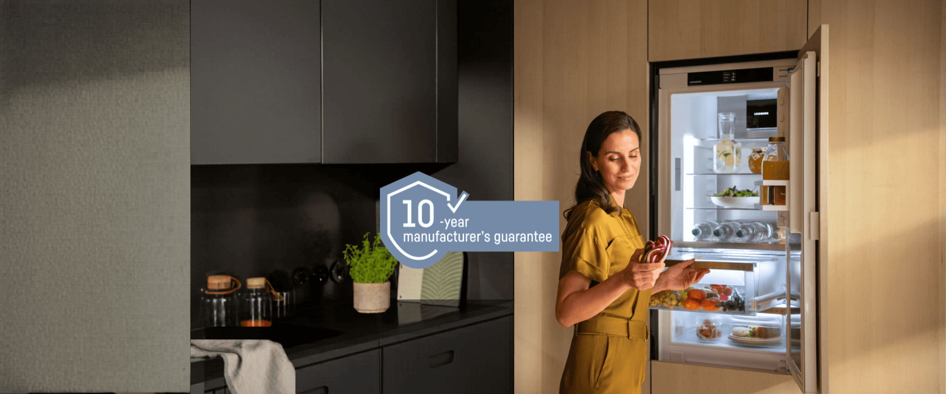 Integrated BioFresh fridge with a 10-year guarantee logo Integrated fridge with BioFresh; a woman stands by an open fridge, holding and looking at a leek. Includes a 10-year guarantee logo, representing a free 10-year guarantee on all household appliances from 1st May to 31st October 2026