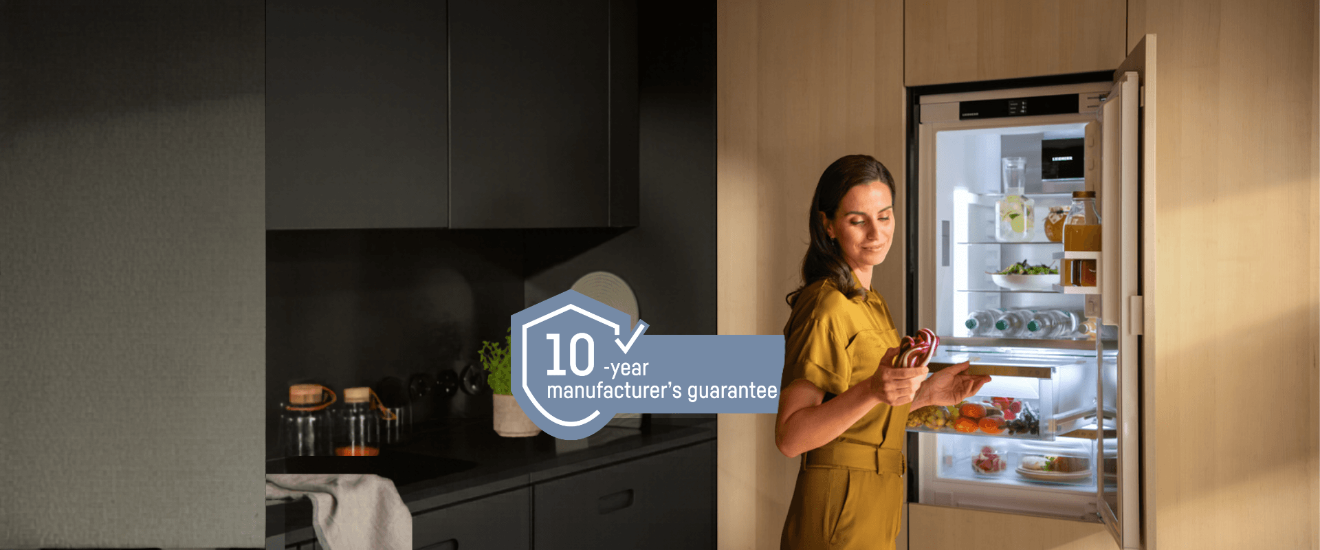 Integrated fridge with BioFresh; a woman opens the drawer, holding and looking at a red cabbage. Includes a 10-year guarantee logo, representing a free 10-year guarantee on all household appliances from 1st May to 31st October 2026.