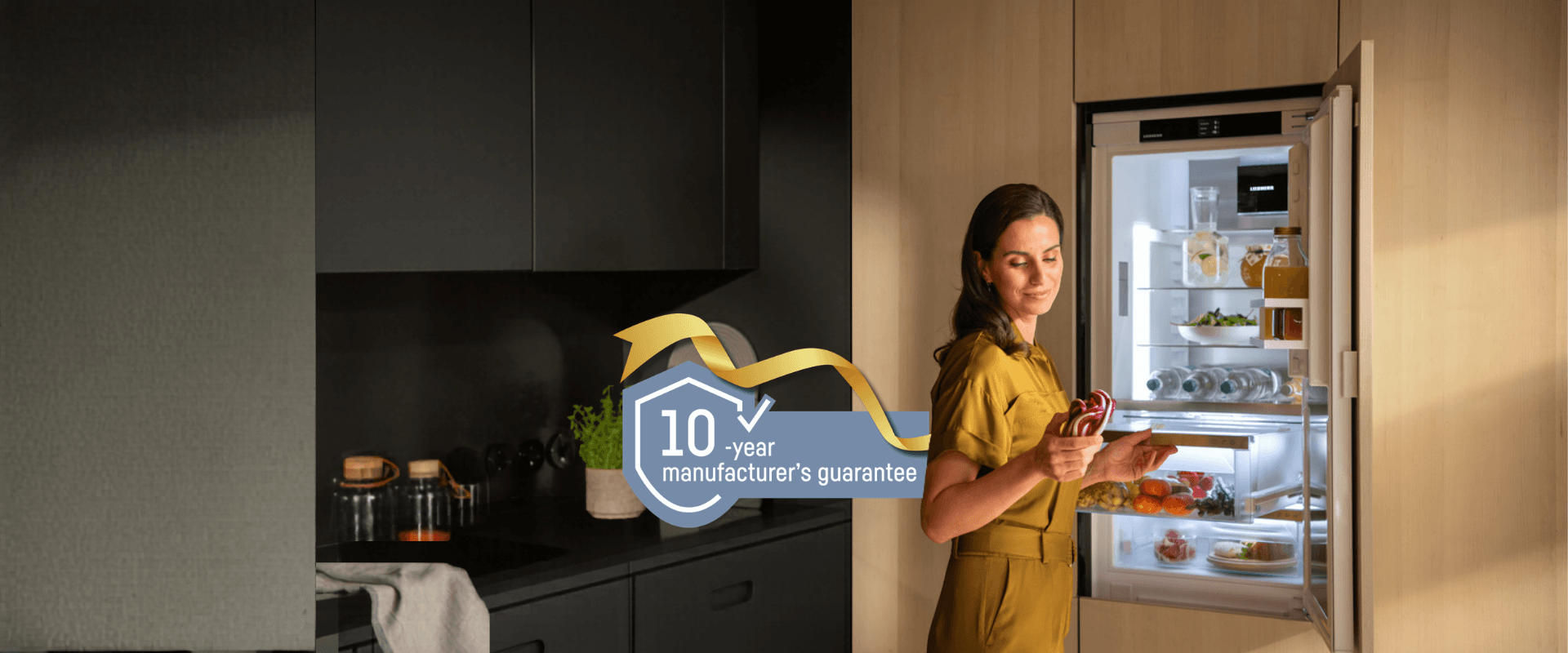 Integrated BioFresh fridge with a 10-year guarantee logo Integrated fridge with BioFresh; a woman opens the drawer, holding and looking at a red cabbage. Includes a gold-ribbon 10-year guarantee logo, representing a free 10-year guarantee on all household appliances from 1st May to 31st October 2026.