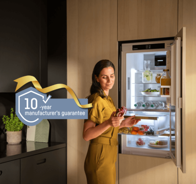 Integrated BioFresh fridge with a 10-year guarantee logo Integrated fridge with BioFresh; a woman opens the drawer, holding and looking at a red cabbage. Includes a gold-ribbon 10-year guarantee logo, representing a free 10-year guarantee on all household appliances from 1st May to 31st October 2026.