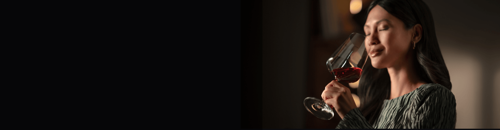 Woman enjoying a glass of wine A woman against a dark background smelling the aromas of a glass of red wine.