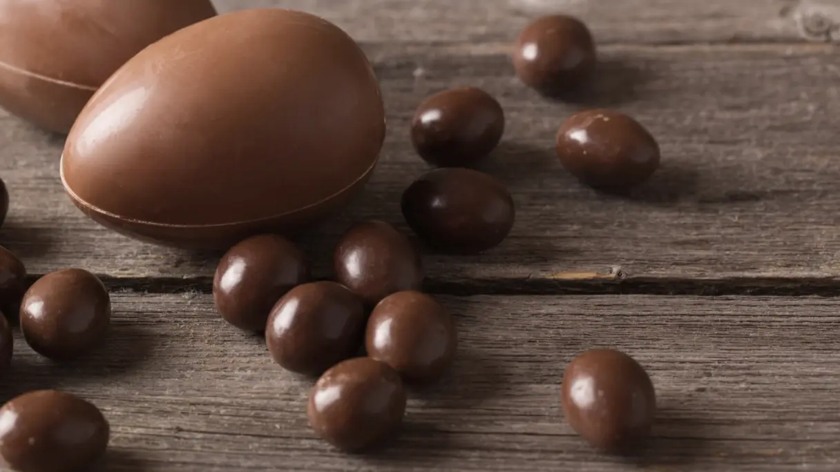 Schokolade lagern und einfrieren Fünf Stücke einer Schokoladentafel mit Haselnüssen sind übereinandergestapelt. Der Untergrund ist blau. Davor liegen Minzblätter und Schokoladensplitter.