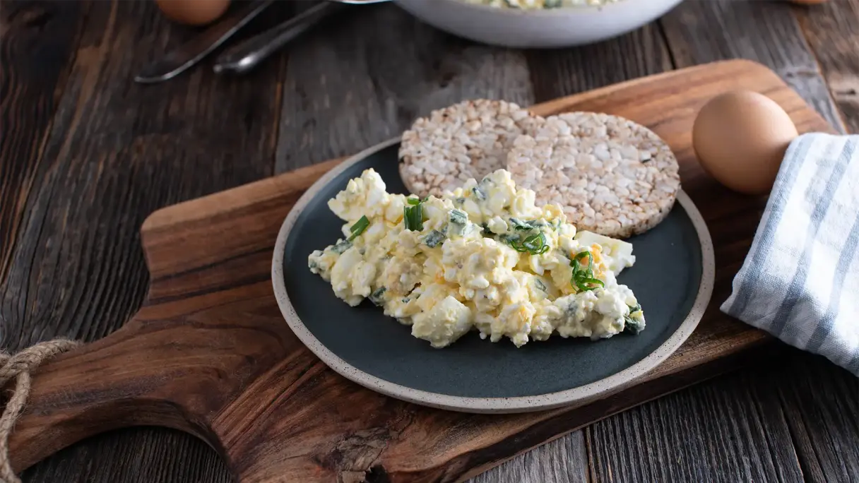 Fettarmer Eiersalat mit körnigem Frischkäse auf einem Teller, serviert mit zwei Reiswaffeln auf Holzbrett.