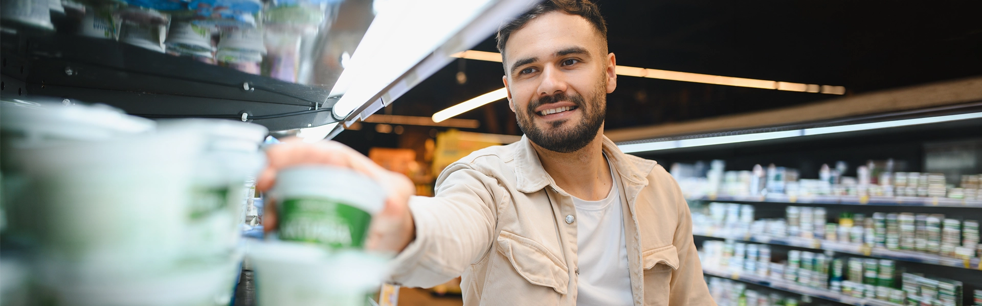Was ist Functional Food? Person greift im Kühlregal eines Supermarkts nach einem Becher; im Vordergrund stehen verschiedene gekühlte Lebensmittelprodukte.