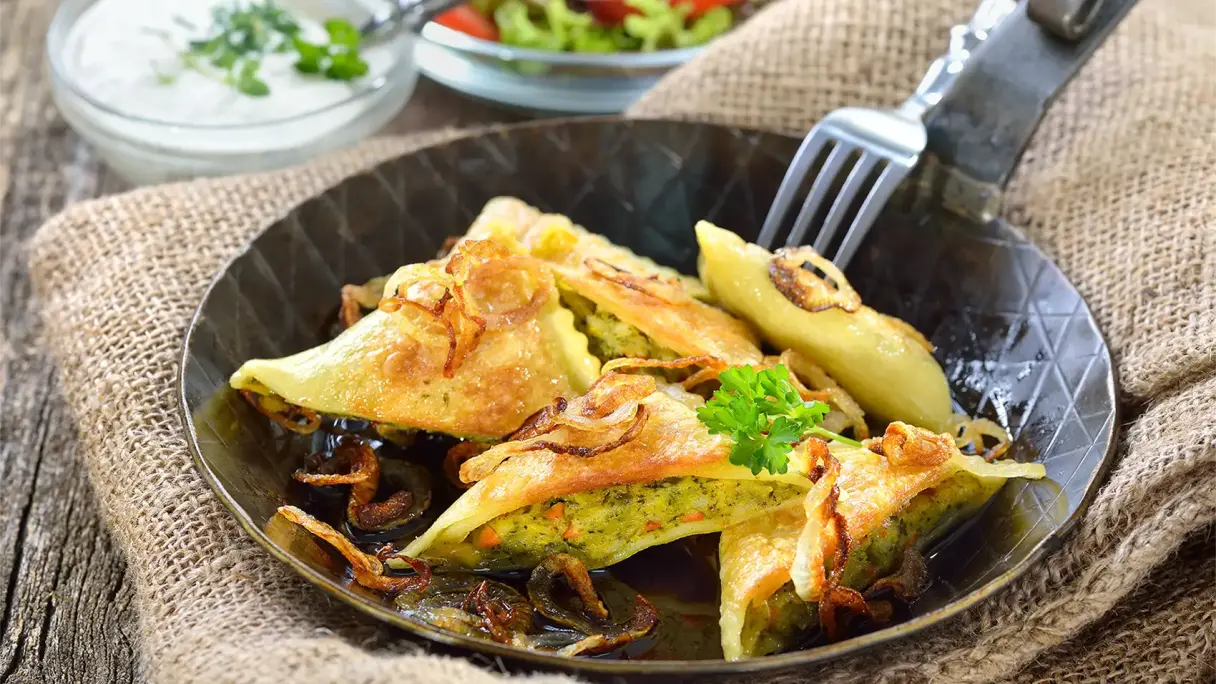 Fried Swabian Maultaschen with crispy onions in a dark pan, garnished with parsley.