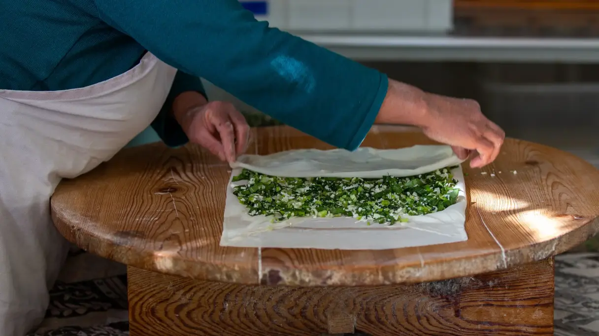 Preparation of Gözleme: thin dough is filled with herbs on a wooden table and carefully folded by hand.