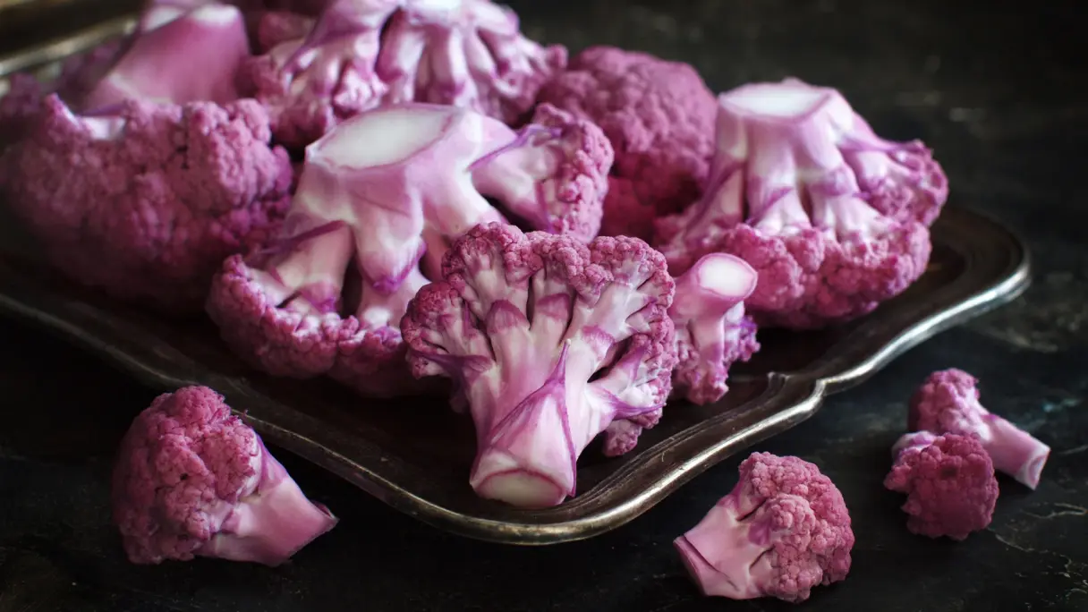 Röschen von violettem Blumenkohl liegen auf einem anthrazitfarbenen Untergrund.