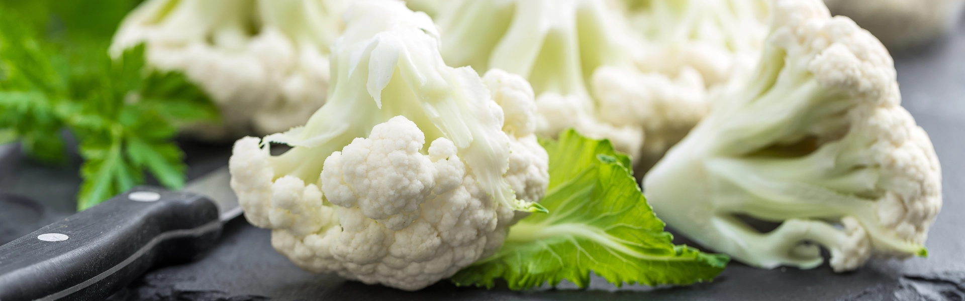 Röschen von weißem Blumenkohl liegen auf einer anthrazitfarbenen Schieferplatte.