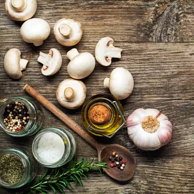 Obenansicht auf ganze und halbe weiße Champignons, die auf einem braunen Holzuntergrund liegen.