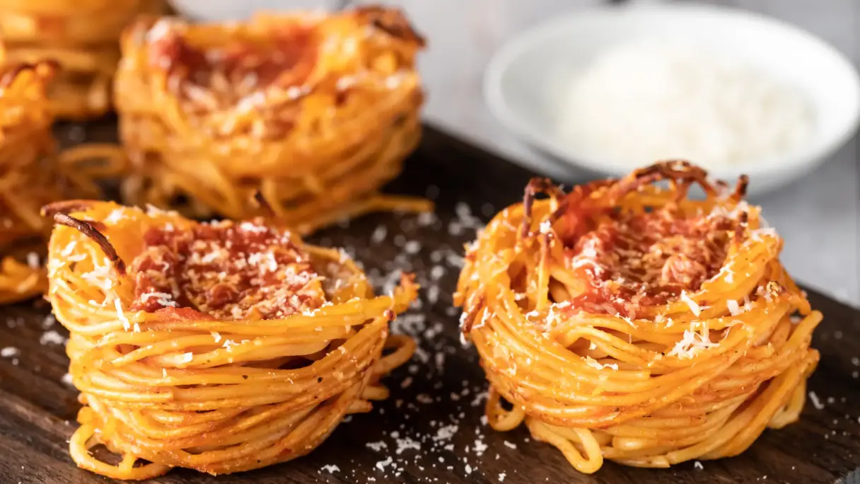 Baked spaghetti muffins with tomato sauce and grated cheese arranged on a wooden board.