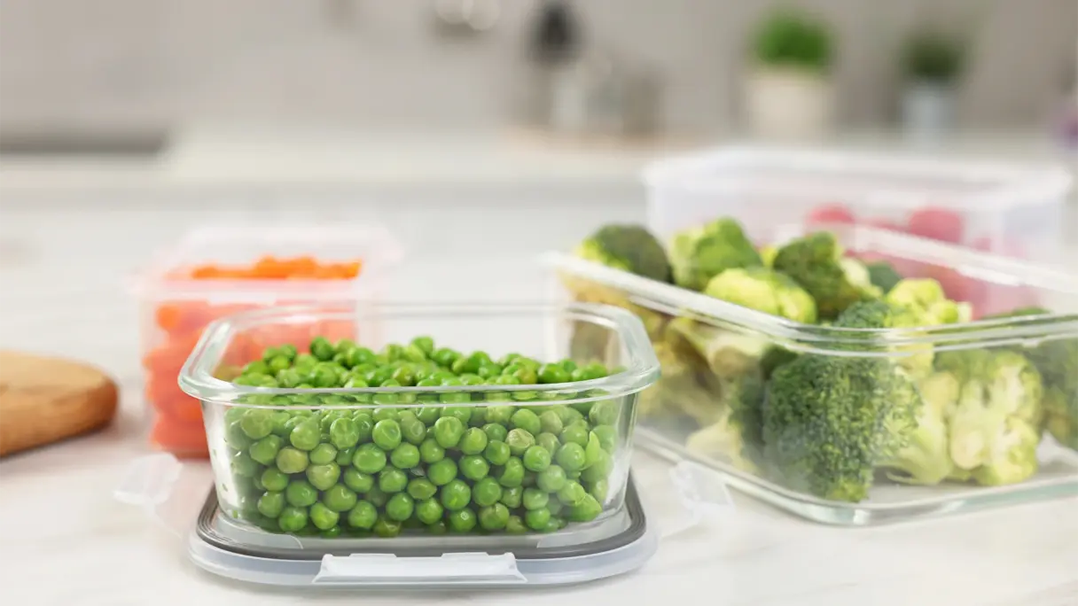 Verschiedene Glasbehälter mit Vakuumdeckeln auf einer Küchenarbeitsplatte, gefüllt mit Brokkoli, Erbsen und Karotten
