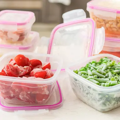 Eine Küchenarbeitsplatte mit verschiedenen Aufbewahrungsboxen, gefüllt mit Gemüse. Im Vordergrund sind zwei geöffnete Behälter mit gefrorenen Tomaten und gefrorenen Bohnen zu sehen.