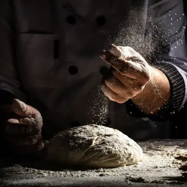 Ein Mann knetet Hefeteig auf einer mit Mehl bestäubten Arbeitsfläche.