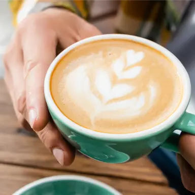 Zwei Hände halten eine Tasse Kaffee mit Latte Art.