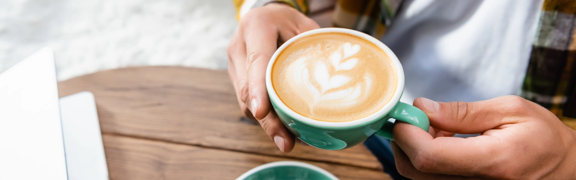 Zwei Hände halten eine Tasse Kaffee mit Latte Art.