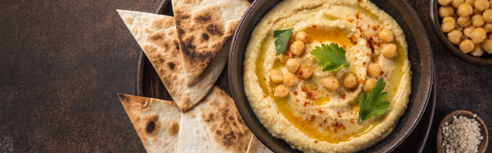 Hummus in einer Schale mit Brotscheiben daneben.