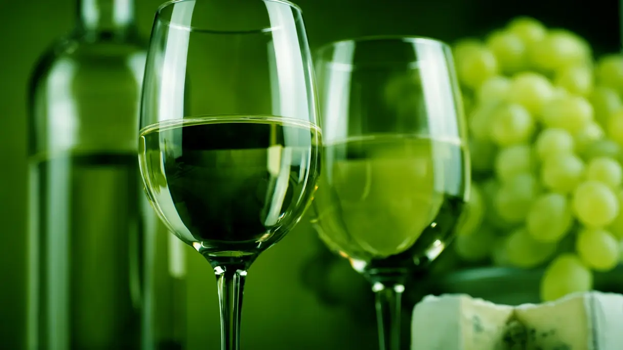 Wie beeinflusst die Lichtfarbe den Geschmack von Wein? Zwei Weingläser im grünen Licht, im Hintergrund eine Weinflasche, Trauben und Weichkäse.