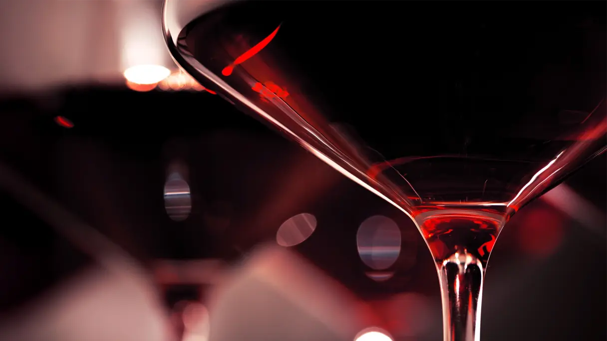 Wie beeinflusst die Lichtfarbe den Geschmack von Wein? Nahaufnahme von Weingläsern mit tiefrotem Rotwein, beleuchtet von rotem Licht.