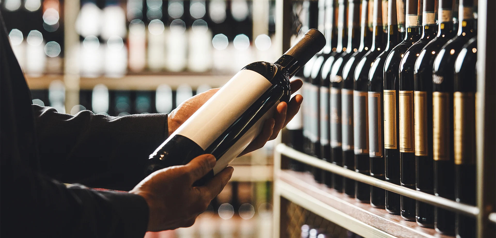 Weinetikett Angaben Person hält Weinflasche vor Weinregal und liest die Beschreibung auf dem Etikett aufmerksam.