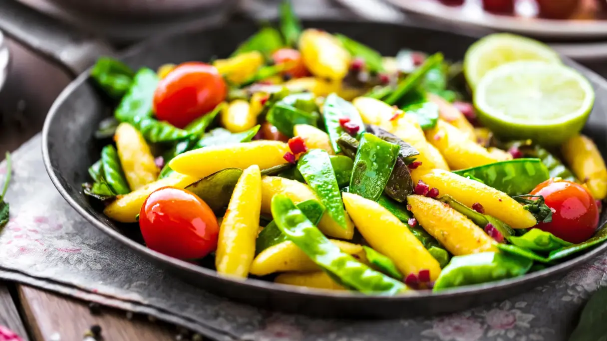 Sugar snap peas cooked in a pan with vegetables and potato noodles.